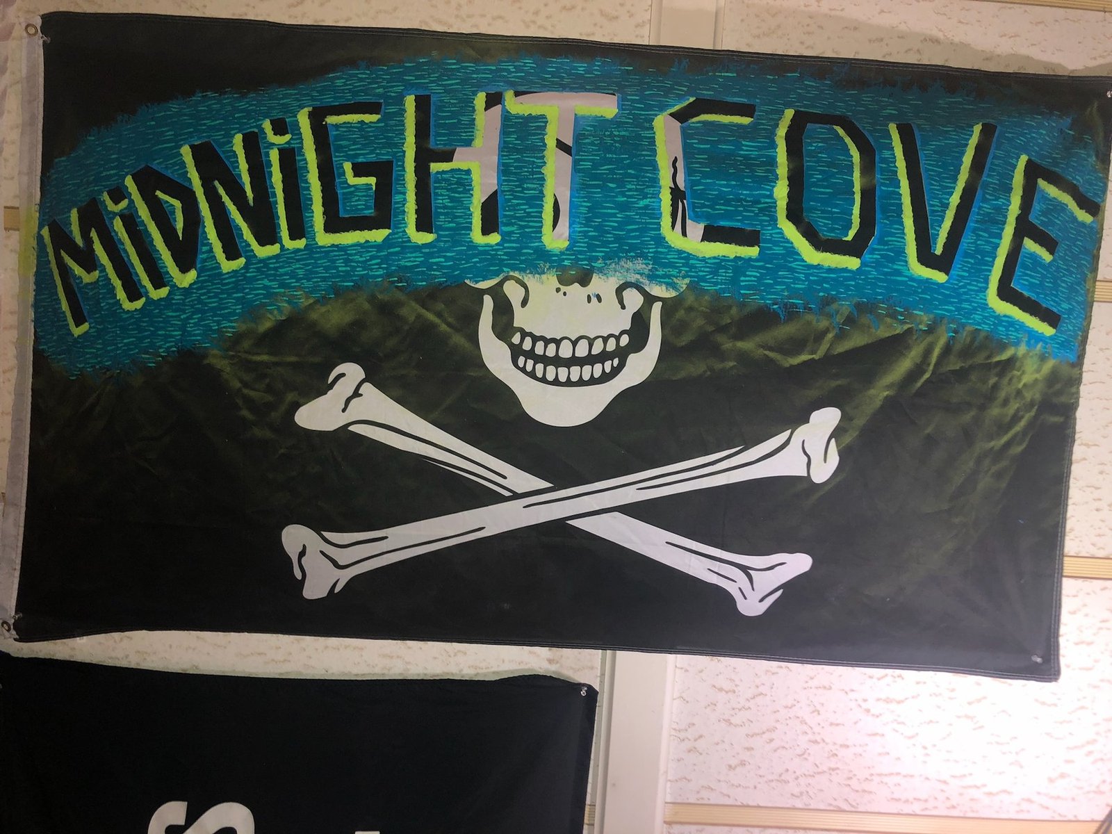 Midnight Cove hand-painted pirate banner — a wavy teal water strip crossing a black flag with the band name in acid-green letters, above a white skull and crossbones